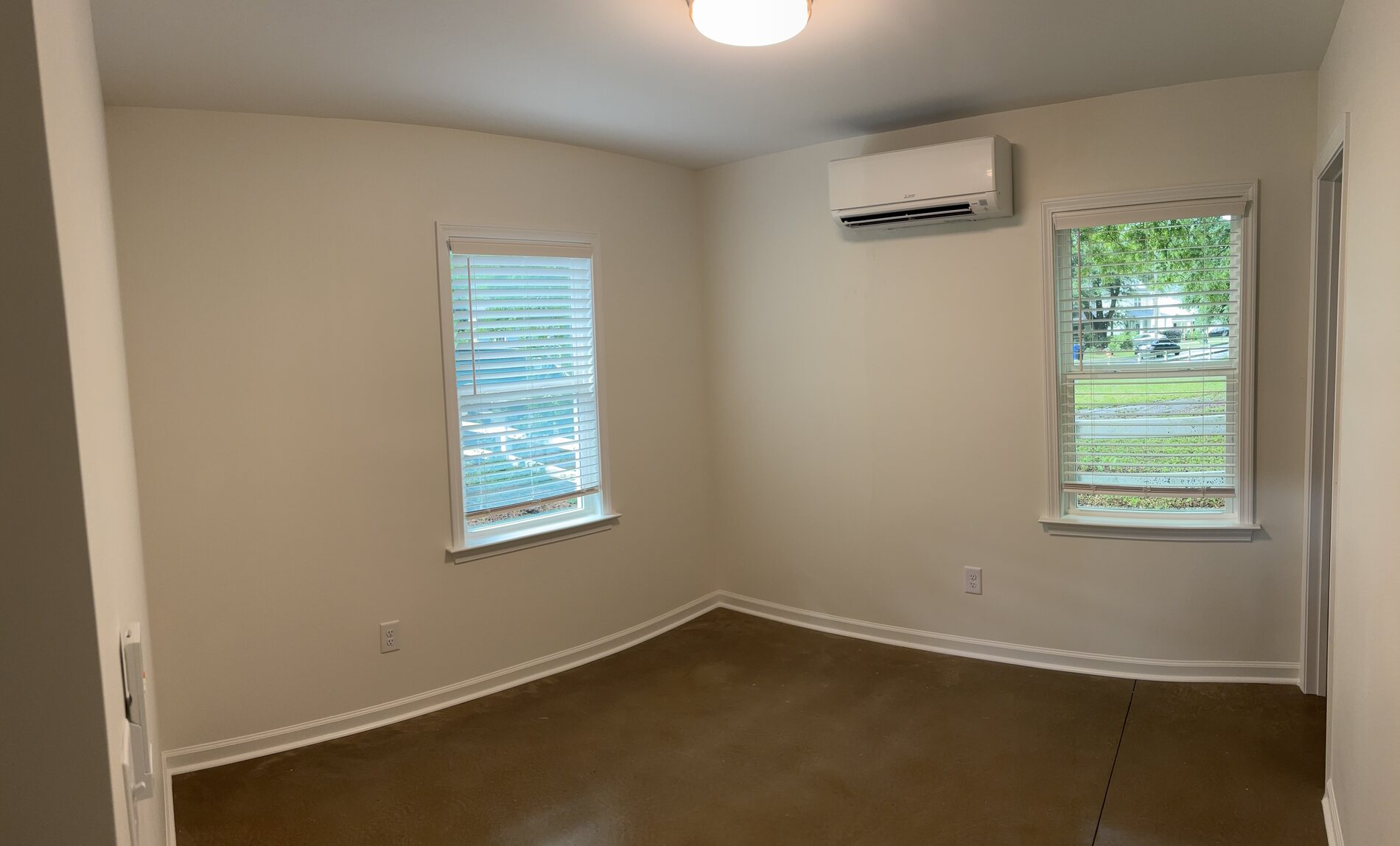 Bedroom with two windows, concrete floor and a wall mounted mini split