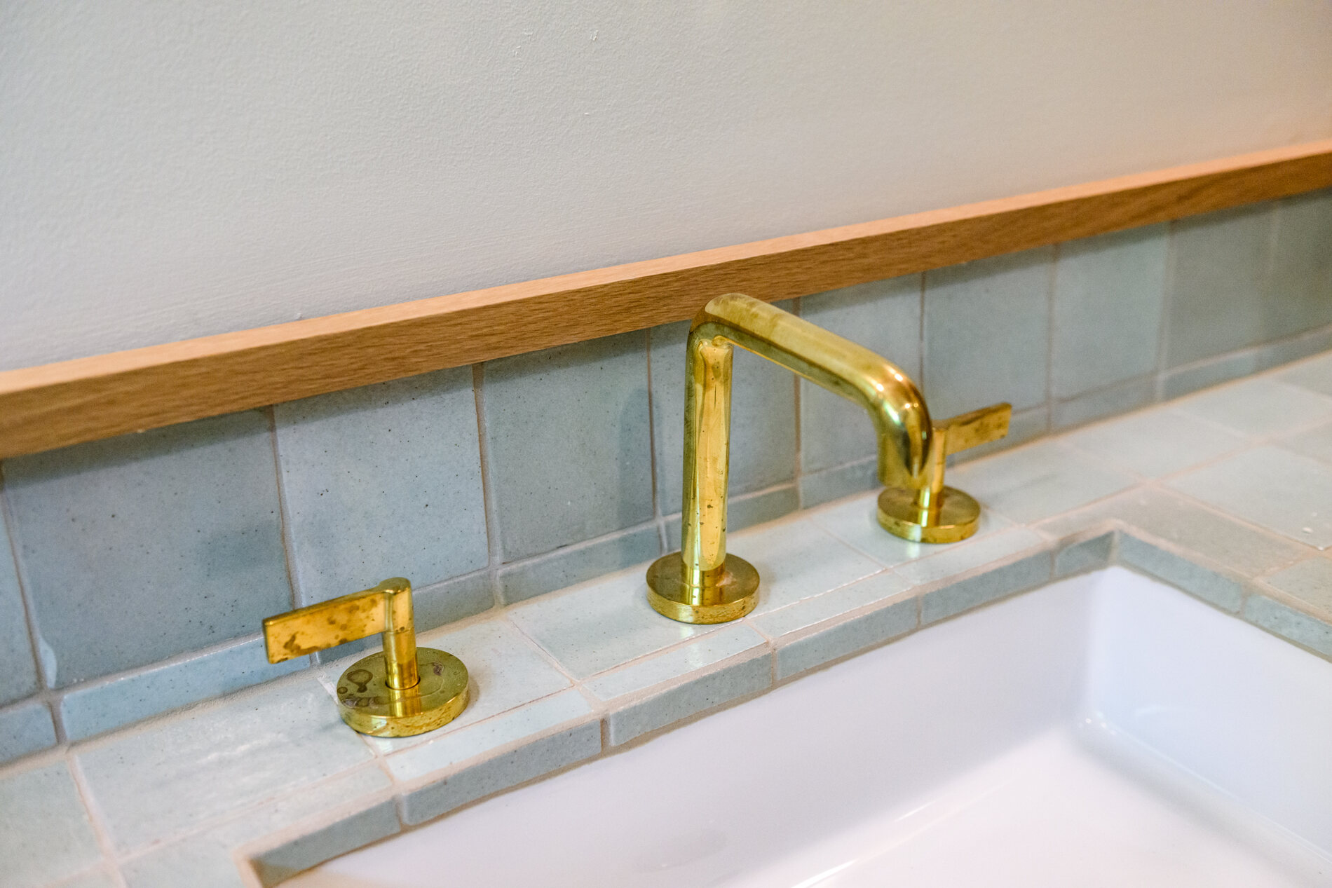Unlacquered brass faucet on a pale blue green tile counter with an undermount sink
