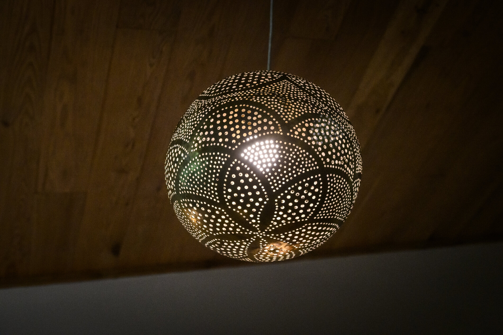 Pierced brass globe pendant hanging below a warm wood ceiling